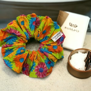 May include: A green, orange, blue, and pink floral print scrunchie with a white tag that reads "Friendship Quilting".