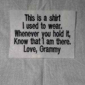 May include: White fabric with a black embroidered message that reads: "This is a shirt I used to wear. Whenever you hold it, know that I am there. Love, Grammy."