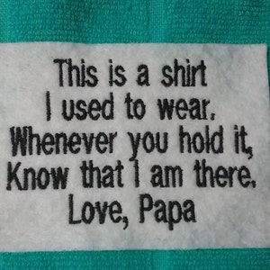 May include: White fabric with black embroidered text that reads: "This is a shirt I used to wear. Whenever you hold it, Know that I am there. Love, Papa."