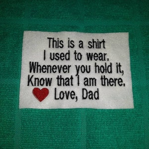 May include: White fabric square with black embroidered text that reads "This is a shirt I used to wear. Whenever you hold it, Know that I am there. Love, Dad". A red heart is embroidered below the text.