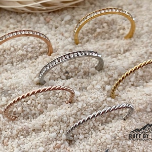 Peut inclure: Cinq anneaux de nez de styles différents. Deux sont en argent avec une rangée de strass clairs. Deux sont en argent et or torsadés. Un est un anneau en or torsadé.