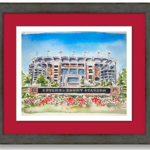 Pu&ograve; includere: Dipinto ad acquerello dello stadio Bryant-Denny, casa della squadra di football americano dei Crimson Tide dell'Universit&agrave; dell'Alabama. Lo stadio &egrave; mostrato frontalmente, con il cartello "Bryant-Denny Stadium" in primo piano.