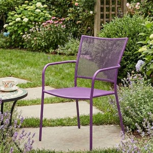 Può includere: Una sedia in metallo viola con schienale a rete e braccioli è posizionata su un sentiero di pietra in un giardino. Un tavolino rotondo con piano a mosaico e una tazza da tè sono nelle vicinanze. Il giardino è fiorito e verde.
