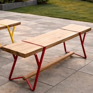 Puede incluir: Dos bancos de madera con asientos de color marrón claro y patas metálicas de colores. Un banco tiene patas amarillas y el otro rojas. Los bancos están al aire libre en un patio embaldosado.