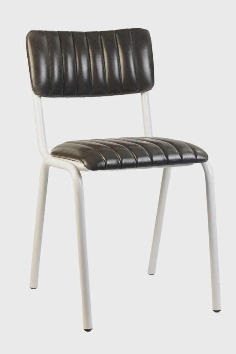May include: A black and white chair with a padded seat and back. The seat and back are black with vertical stitching. The frame is white and made of metal. The chair has four legs.