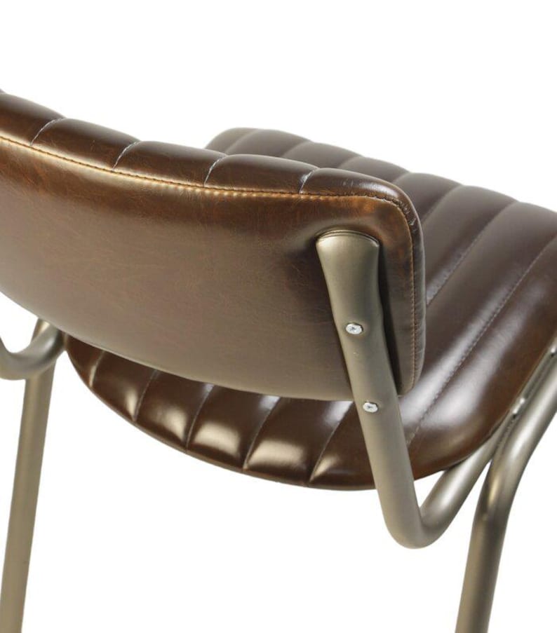 May include: Close-up of a brown leather chair with a curved back and seat. The chair has a metal frame with visible rivets. The leather is stitched with a quilted pattern, and the metal has a brushed finish.