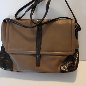 May include: A brown leather shoulder bag with a flap closure and a long, adjustable strap. The bag features dark brown crocodile-textured accents on the corners and strap details. The bag is designed with a buckle closure and a top handle.
