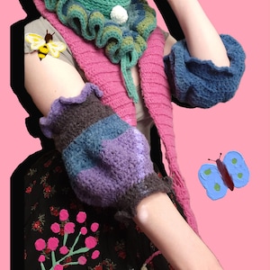 Puede incluir: Una bufanda de ganchillo colorida con un borde rizado y un pompón blanco. La bufanda se combina con un calientamanos de ganchillo en un patrón a rayas de morado, azul y marrón. El calientamanos también tiene un borde rizado. La imagen incluye una abeille y una mariposa pintadas.