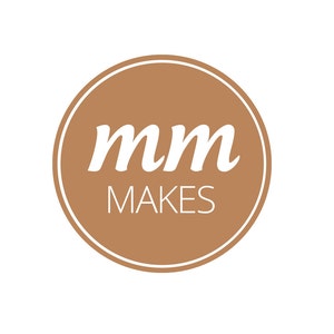Può includere: Un cerchio marrone con un contorno bianco e il testo "mm MAKES" in bianco.