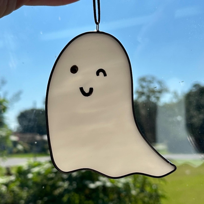 May include: A white ghost with a black outline, winking and smiling. The ghost is hanging from a black string.