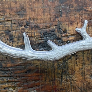 May include: A silver metal branch with a textured surface, resembling a tree branch.