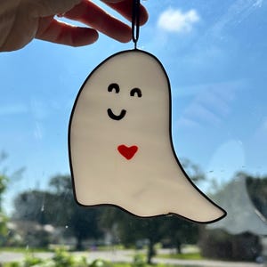 May include: A white ghost with a black outline and a red heart. The ghost has a smiling face with black eyes and a black mouth.