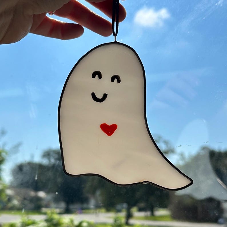 May include: A white ghost with a black outline and a red heart. The ghost has a smiling face with black eyes and a black mouth.