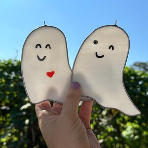 May include: Two white stained glass ghosts with black eyes and smiles. One ghost has a red heart on its chest.