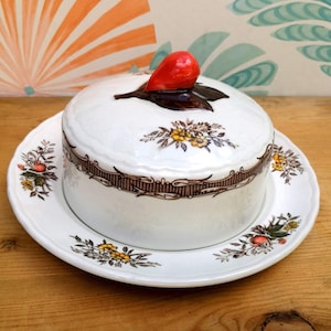 May include: A white ceramic butter dish with a floral design and a red and brown leaf-shaped lid. The dish has a matching plate.