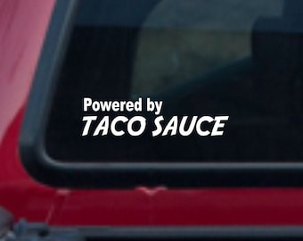 May include: A red pickup truck with a black tailgate and a white vinyl sticker on the back window that says "Powered by Taco Sauce".