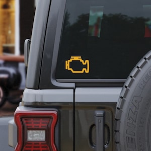 May include: A black SUV with a yellow check engine light sticker on the rear window. The sticker is a stylized icon of a car engine with a wrench on top.