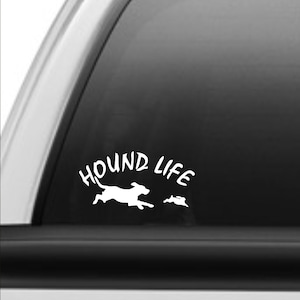 May include: White vinyl decal with the text "Hound Life" and a silhouette of a dog running with a rabbit. The decal is on the back window of a gray pickup truck.