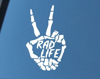 May include: White vinyl decal of a skeleton hand making the peace sign with the words "RAD LIFE" written inside the hand.