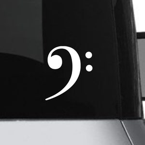 May include: A white bass clef vinyl sticker on a gray car window.