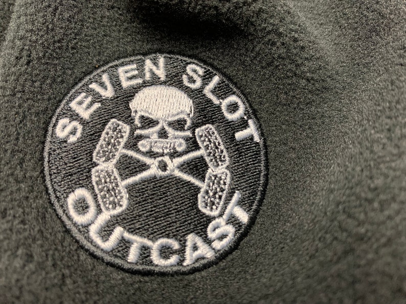 May include: A black and white embroidered patch with a skull and crossbones design. The patch reads "Seven Slot Outcast".
