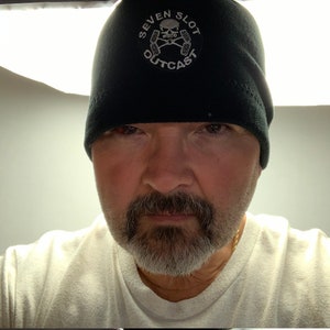 May include: A man wearing a black beanie with a white skull and crossbones logo that says "Seven Slot Outcast".