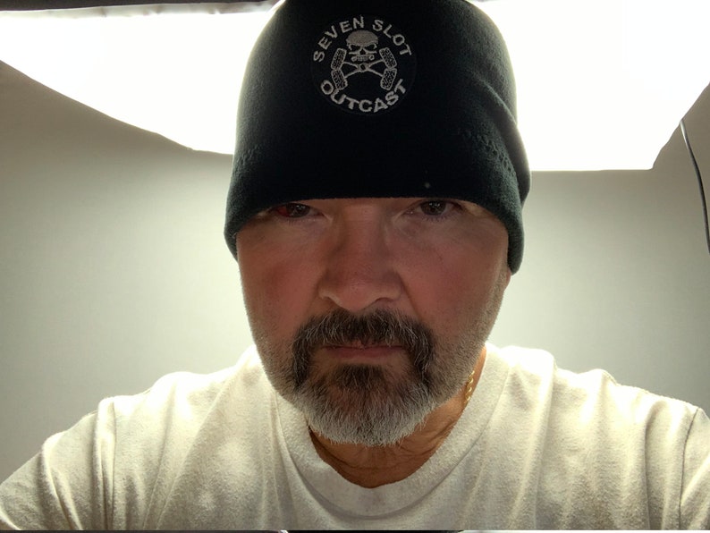 May include: A man wearing a black beanie with a white skull and crossbones logo that says "Seven Slot Outcast".