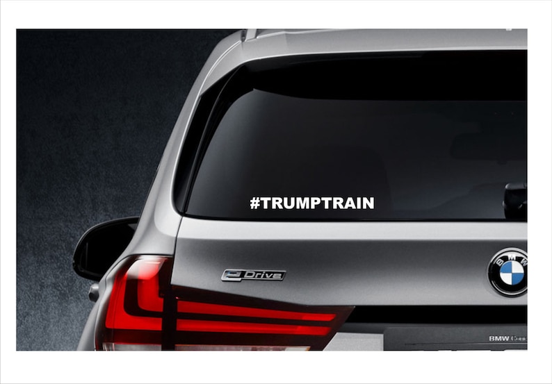 May include: A silver car with a white decal on the rear window that says "#TRUMPTTRAIN".