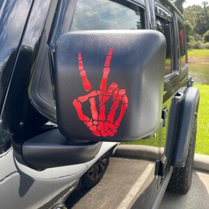 May include: A black car side mirror with a red skeleton hand peace sign sticker.
