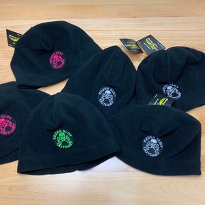 May include: Five black fleece beanies with a skull and crossbones logo that says "Seven Slot Outcast". The logos are in different colors, including pink, green, and white.