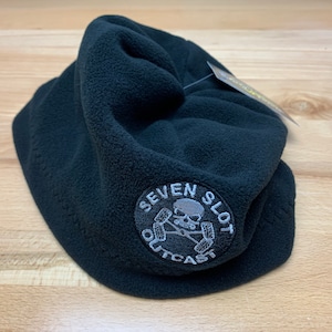 May include: Black fleece beanie with a white embroidered logo that says "Seven Slot Outcast" with a skull and crossbones design.