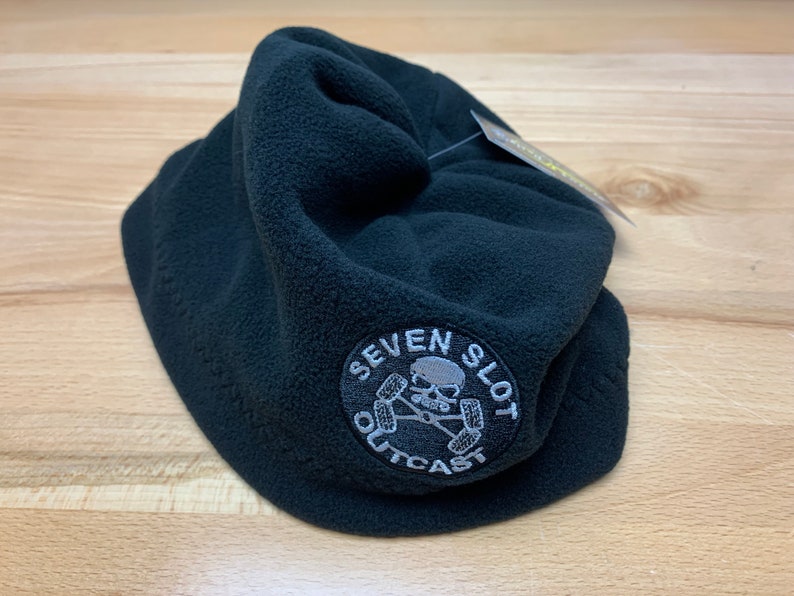 May include: Black fleece beanie with a white embroidered logo that says "Seven Slot Outcast" with a skull and crossbones design.