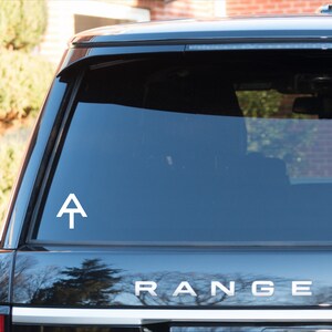 May include: A white vinyl sticker with the Appalachian Trail logo, a white triangle with a white line across the middle, on the rear window of a black SUV. The SUV has the word "RANGER" in silver letters on the back.