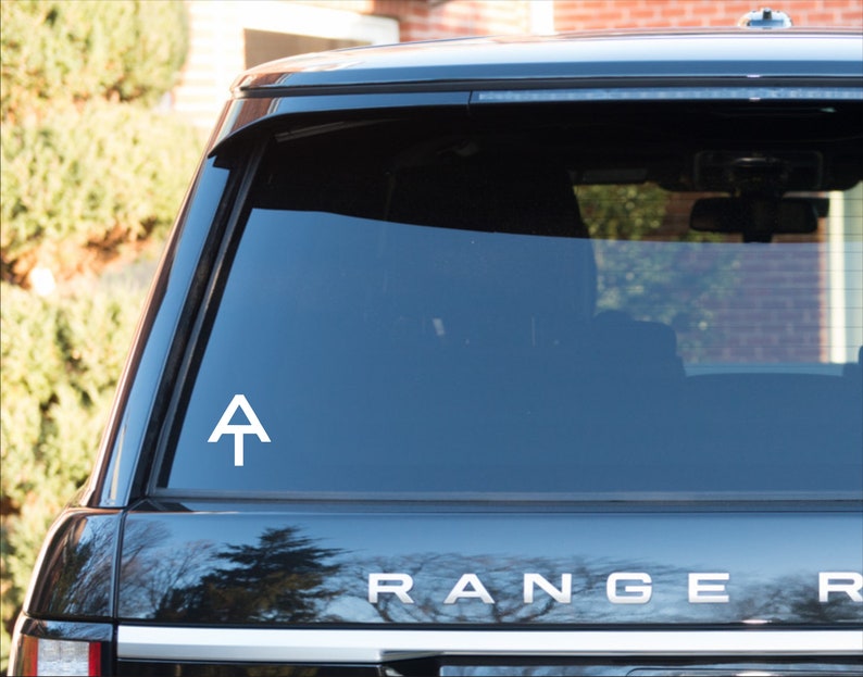 May include: A white vinyl sticker with the Appalachian Trail logo, a white triangle with a white line across the middle, on the rear window of a black SUV. The SUV has the word "RANGER" in silver letters on the back.