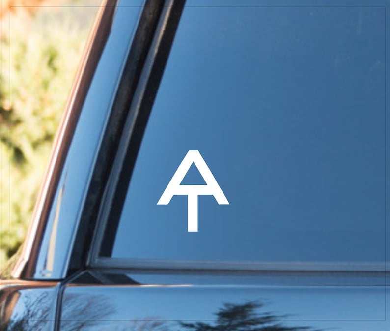 May include: White vinyl decal of the letter "A" with a horizontal line through the middle, resembling a mountain peak. The decal is on a blue car window.