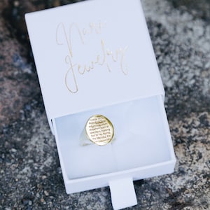 May include: A gold ring with an inscription in a white box. The inscription reads: "I came forth from Godland detached from all save Him holding fast to Ha Name, the Meradu, the Compassionate."