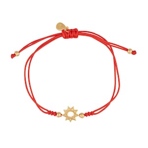 May include: A red string bracelet with a gold sun charm. The bracelet is adjustable and has a small gold bead at each end.