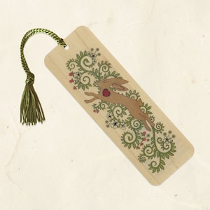 May include: A wooden bookmark with a green tassel. The bookmark features a brown rabbit with a red heart jumping through a green leafy vine with white flowers.