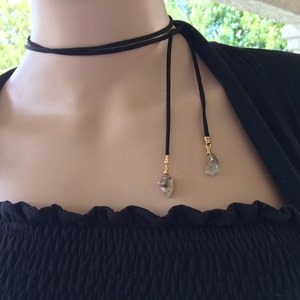 May include: A black suede choker necklace with two long ties and gold-toned charms featuring clear quartz crystals.