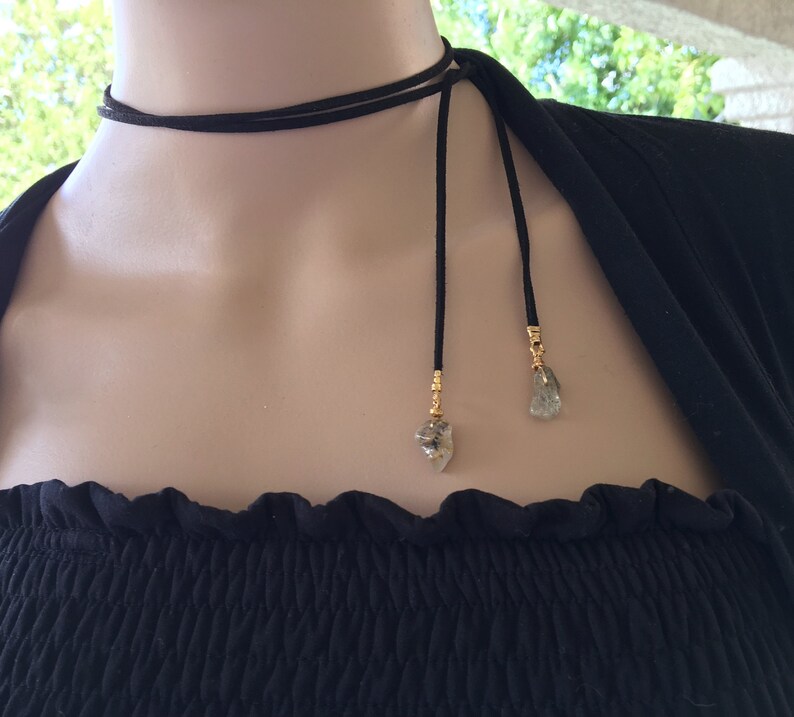 May include: A black suede choker necklace with two long ties and gold-toned charms featuring clear quartz crystals.