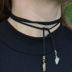 May include: A black choker necklace with two crystal pendants. The necklace is made of suede and has a simple design.