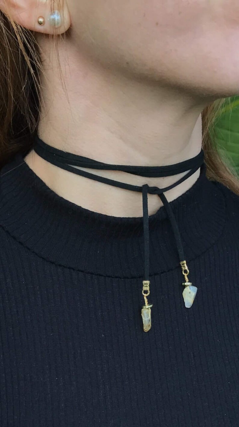 May include: A black choker necklace with two crystal pendants. The necklace is made of suede and has a simple design.