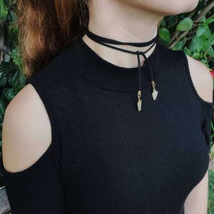 May include: A black choker necklace with two small, light-colored stones hanging from it. The necklace is worn by a person with red hair.