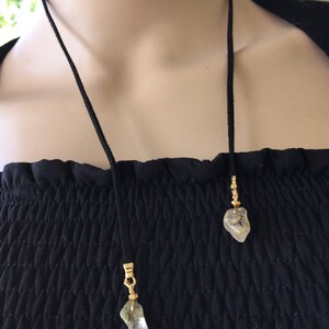 May include: A black suede cord necklace with two gold-toned pendants featuring clear, irregularly shaped stones.
