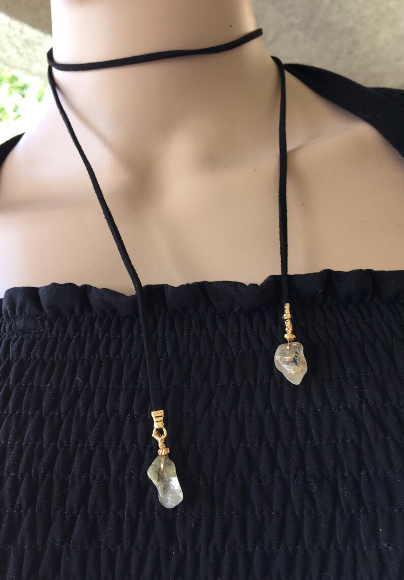 May include: A black suede cord necklace with two gold-toned pendants featuring clear, irregularly shaped stones.