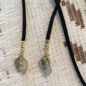 May include: Two black suede cords with gold metal accents and clear quartz crystals attached to the ends.
