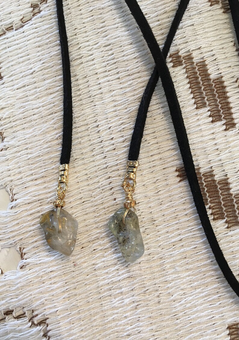 May include: Two black suede cords with gold metal accents and clear quartz crystals attached to the ends.