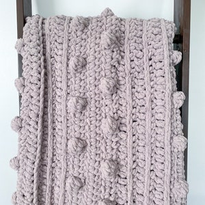 May include: A soft, plush, mauve-colored knitted throw blanket with a textured, bobble stitch pattern.