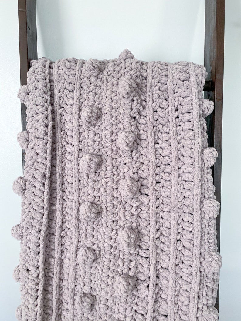 May include: A soft, plush, mauve-colored knitted throw blanket with a textured, bobble stitch pattern.