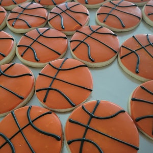 May include: A tray of round cookies decorated to resemble basketballs. Each cookie has an orange icing base with black icing lines to mimic the ball's design. The cookies are arranged in neat rows.